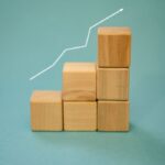 Home Wooden blocks forming a staircase with an upward arrow symbolizing growth and progress.